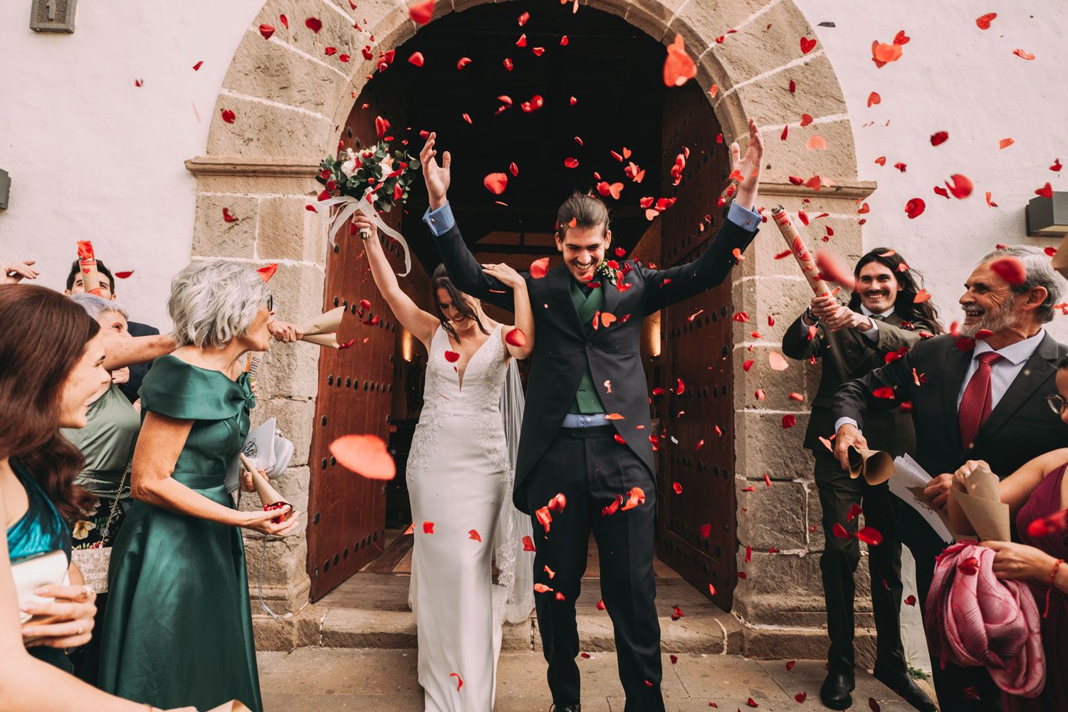 Boda en Tenerife: novios saliendo de la iglesia entre pétalos de rosas rojas mientras los invitados celebran