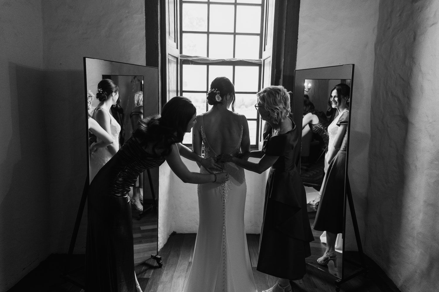 Novia siendo ayudada a vestirse antes de la ceremonia, retrato en blanco y negro frente a un espejo